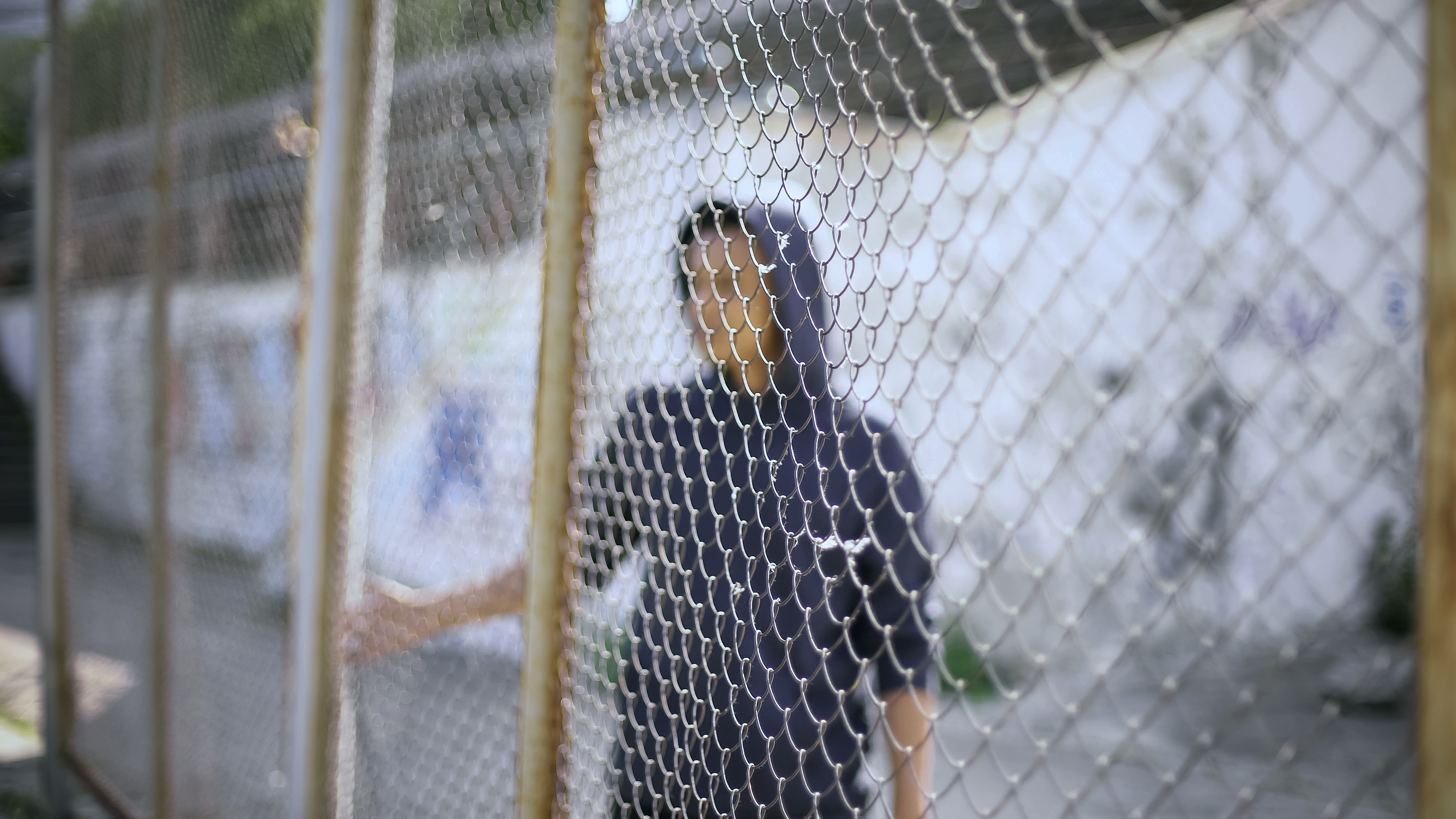 young man of color wearing a hoodie behind a cyclone fence