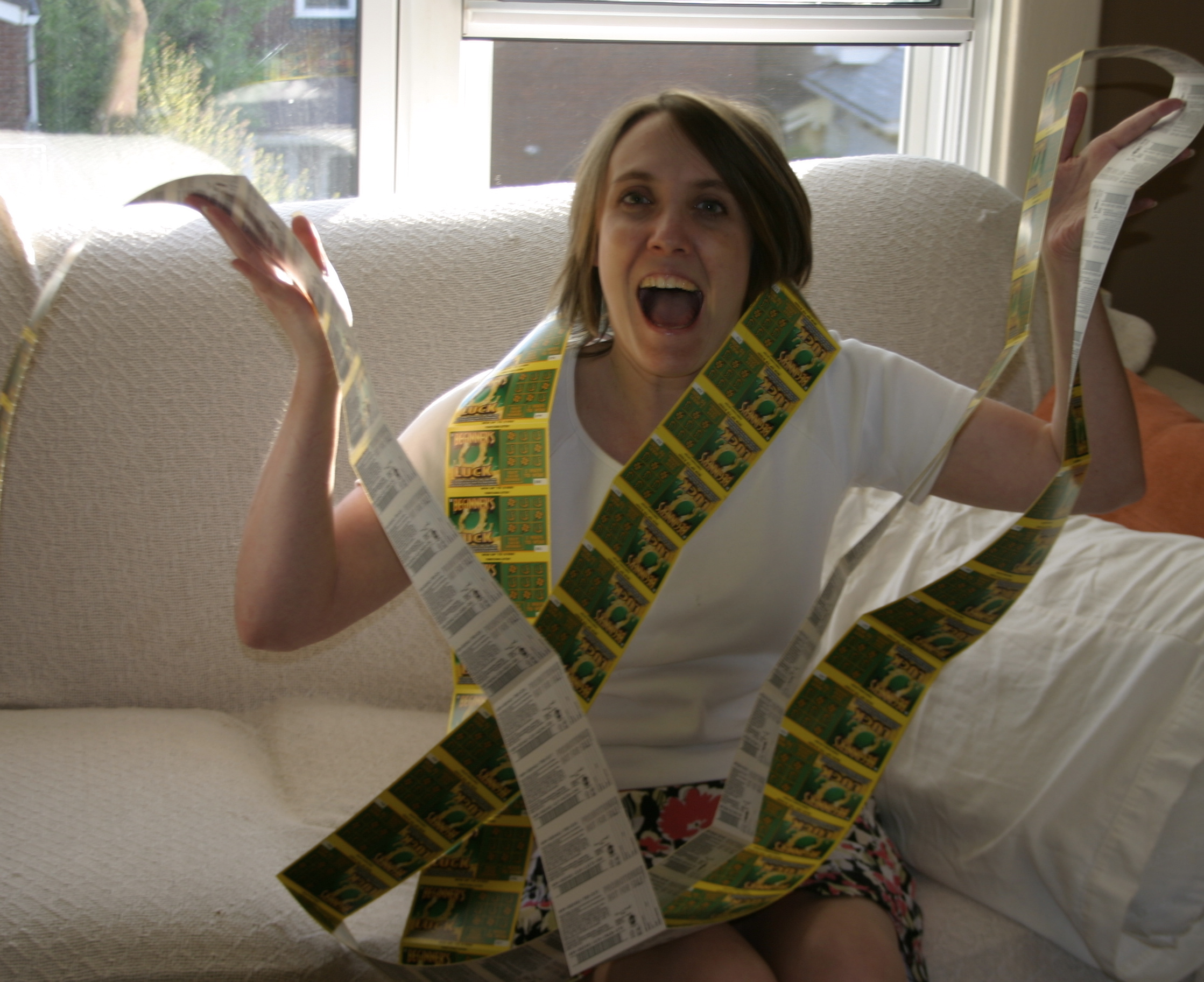 A white woman is wrapped in Lottery scratchers, with a big smile.