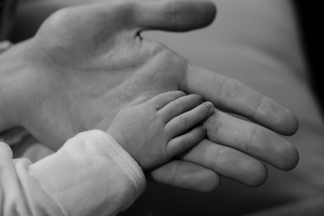 Black and white photo of a child's hand touching a parent's palm.