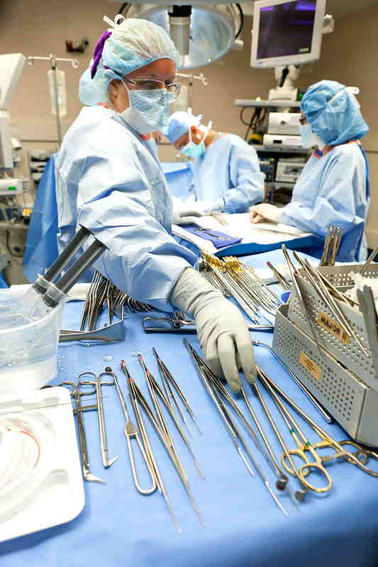 Surgeon in blue scrubs reaching for surgical tools laid on a blue surface