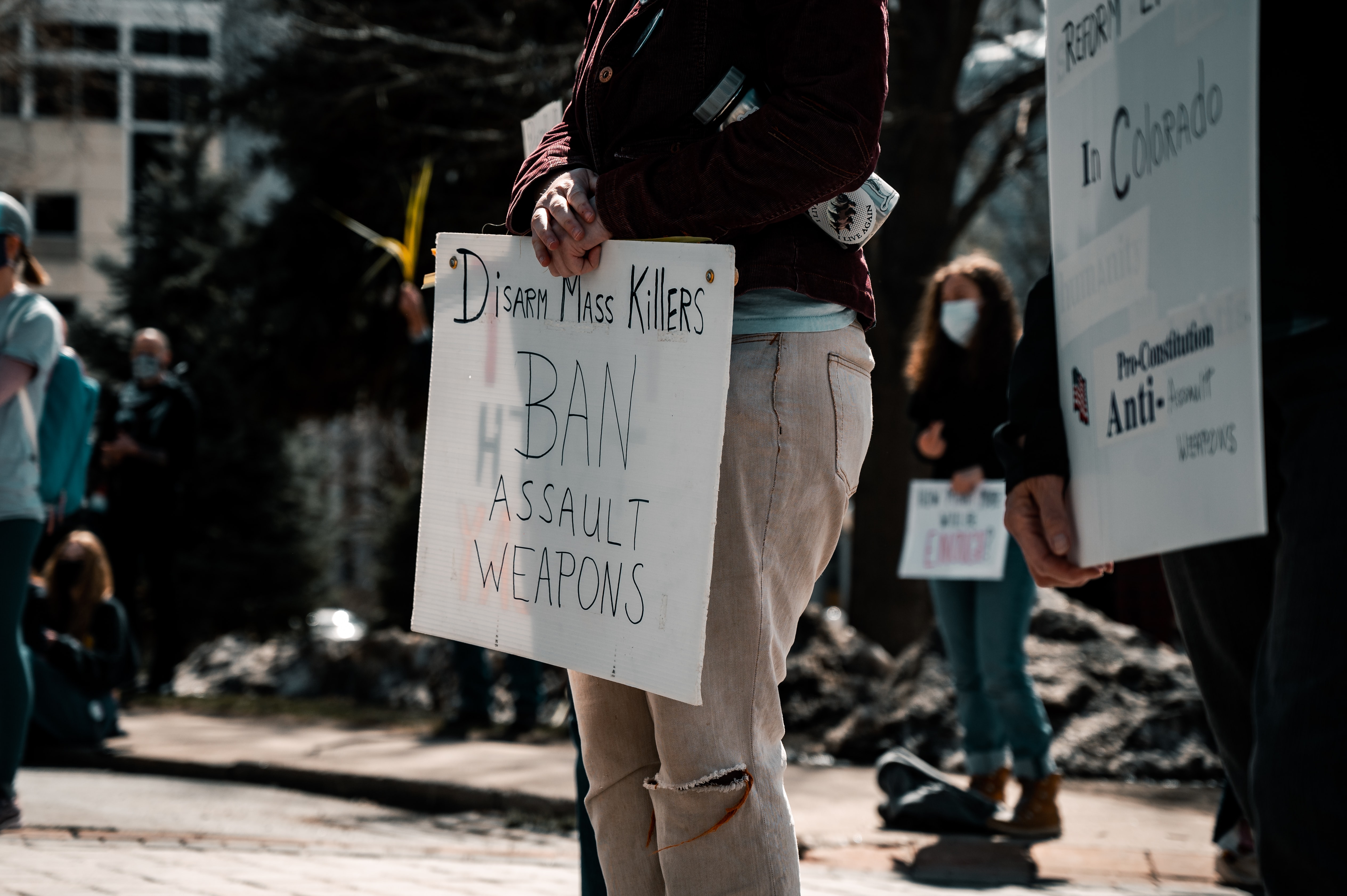 a person holding a white protest sign that says "disarm mass killer ban assault weapons" this is at a protest