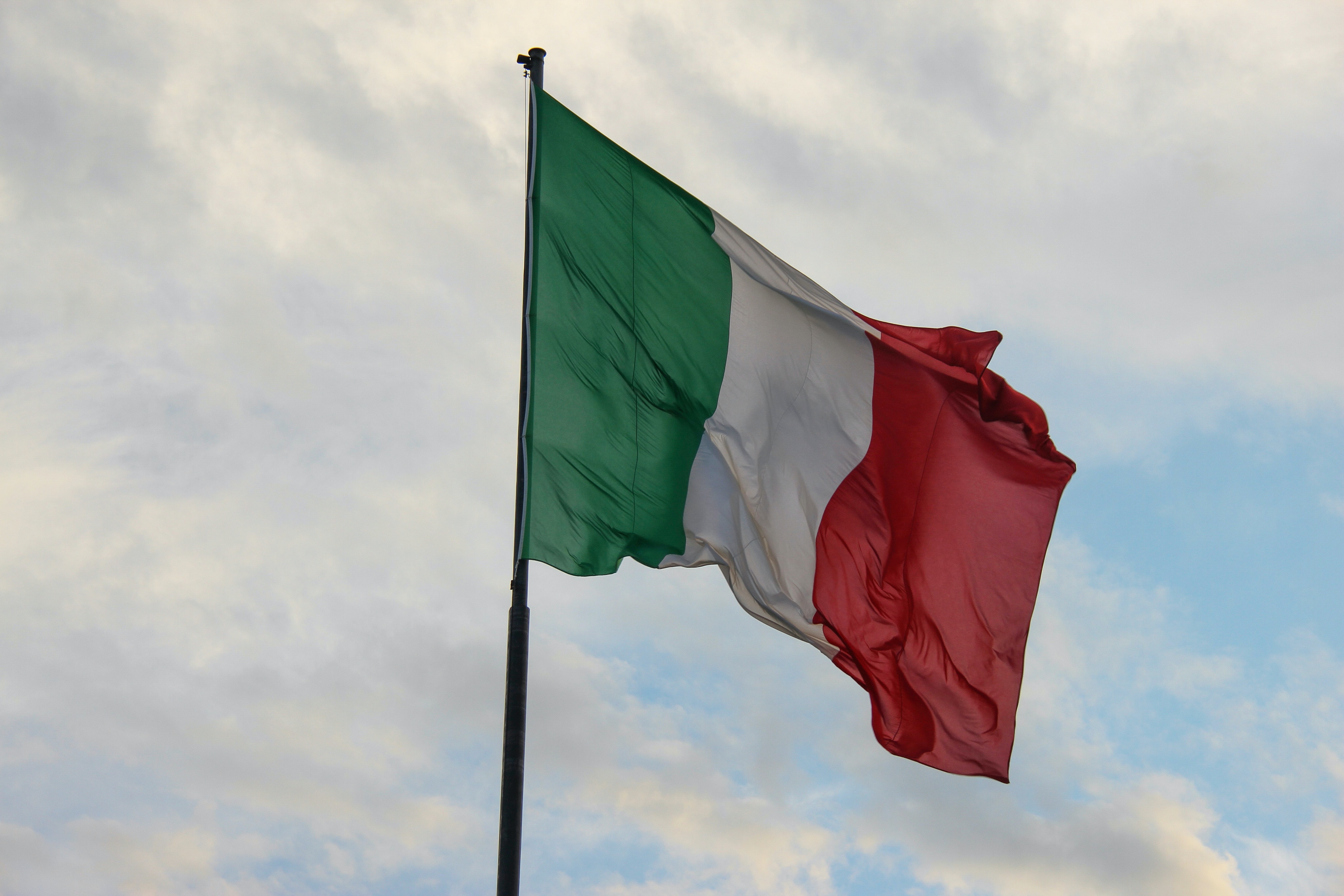 Italian red white and green flag against blue sky and clouds background