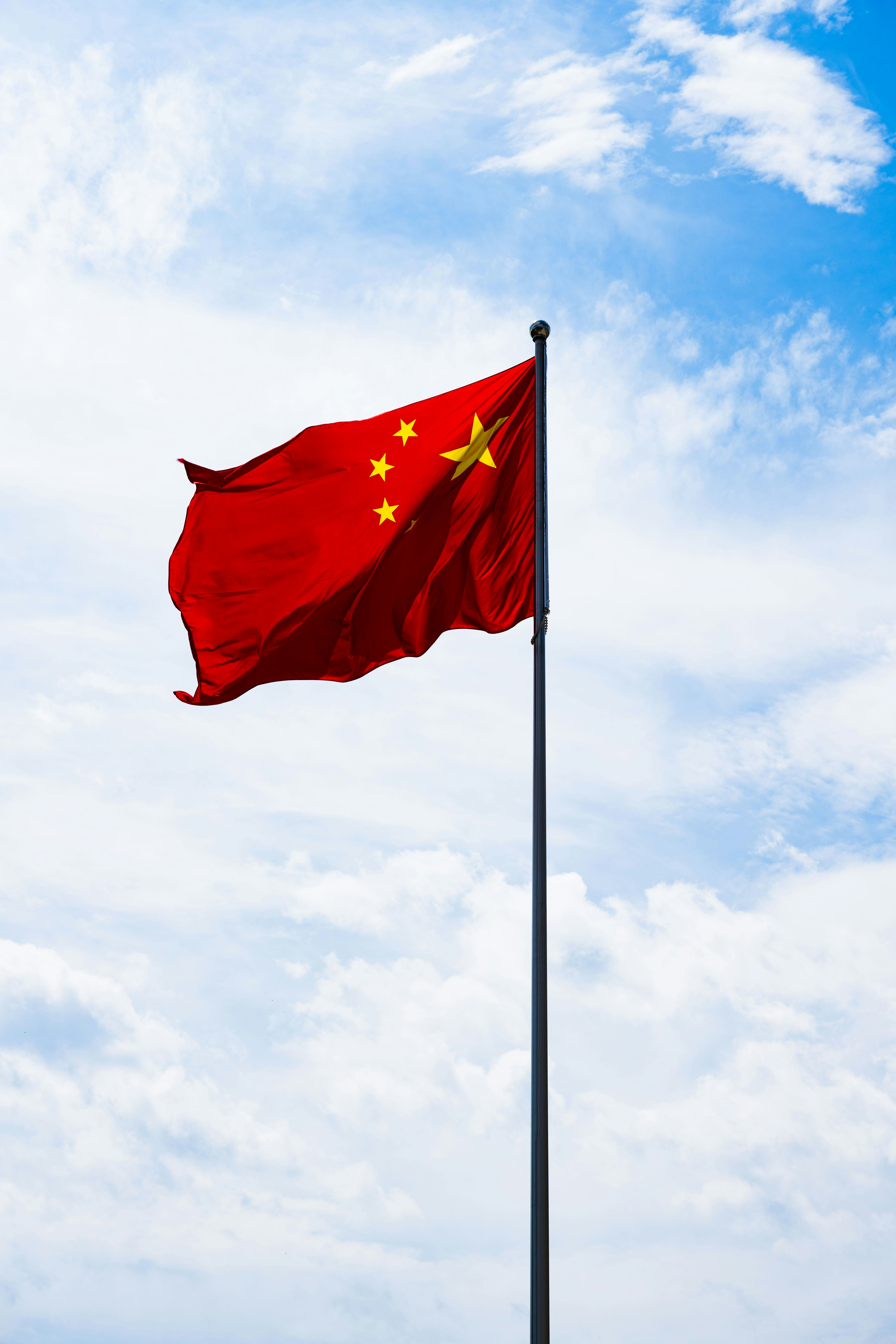 Chinese flag on flagpole with blue sky and clouds in background