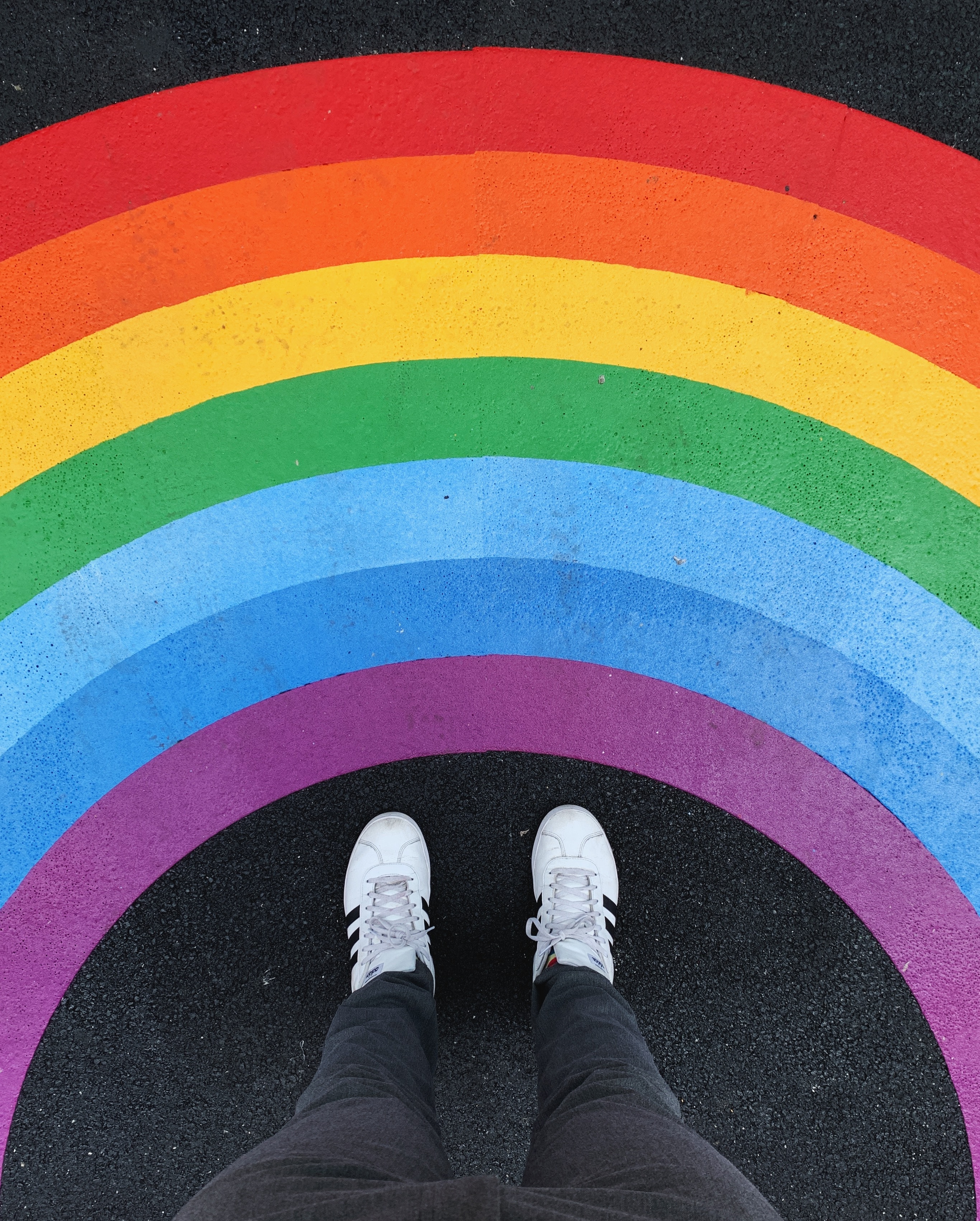 image of two white shoes below a chalk like image of a rainbow on the floor