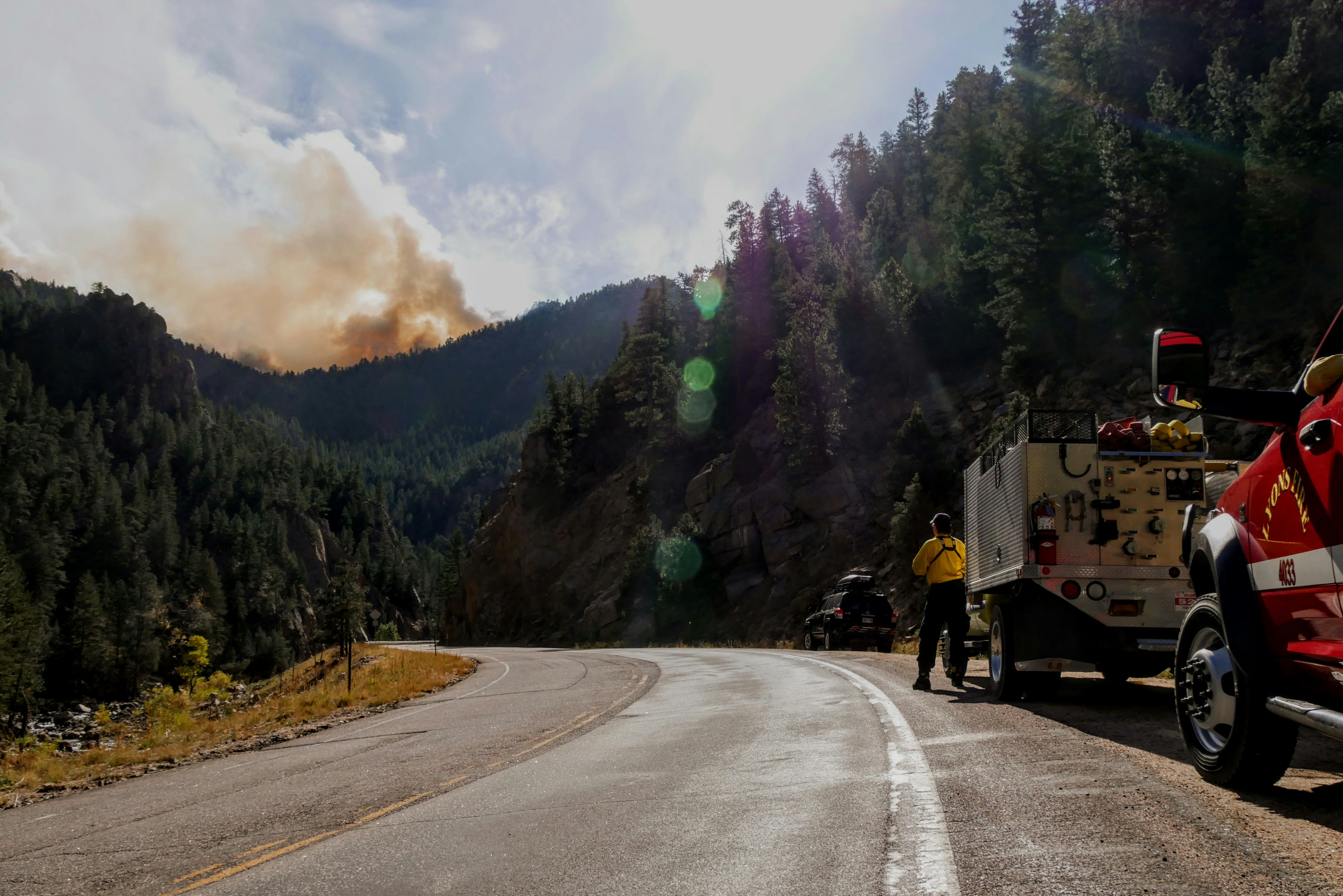 a photo of a highway in California with a firetruck and a fire in the trees in the distance