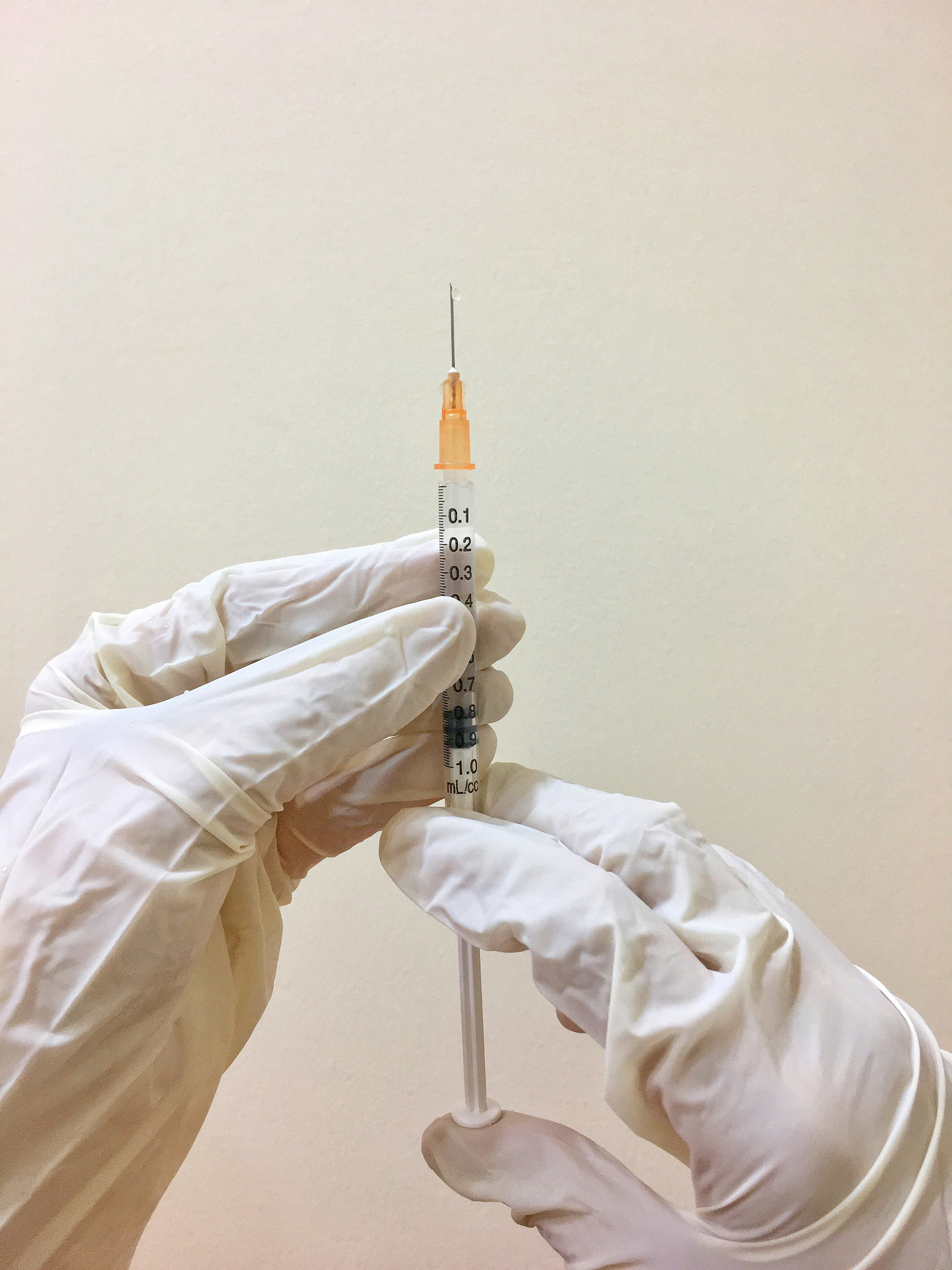 two gloved hands hold a vaccine in a syringe
