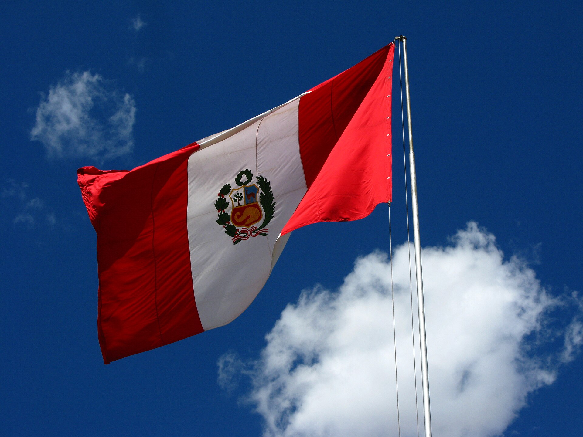 flag of Peru on flagpole with blue sky and clouds in the background