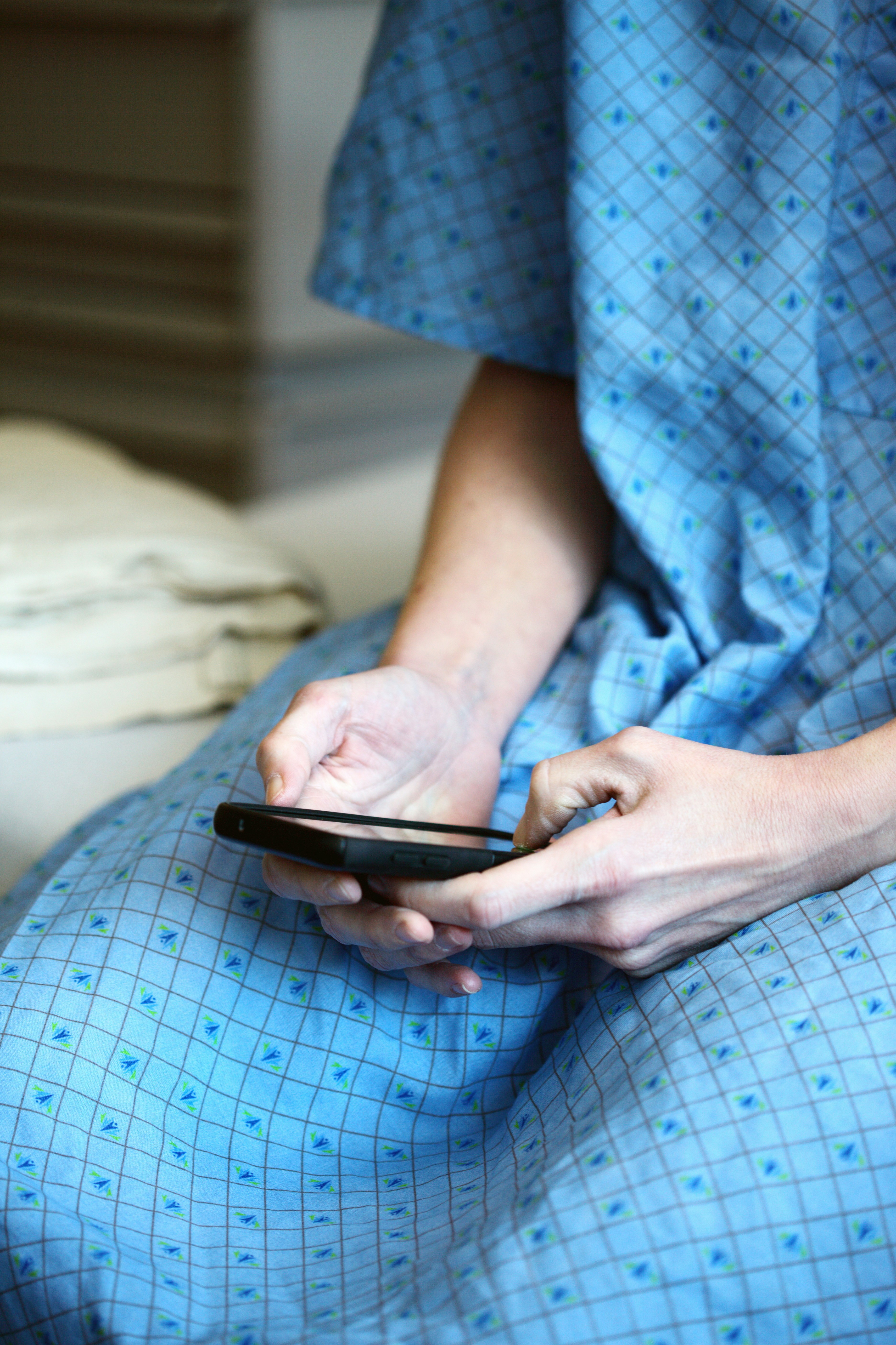 a person wearing a hospital gown looks at a smartphone