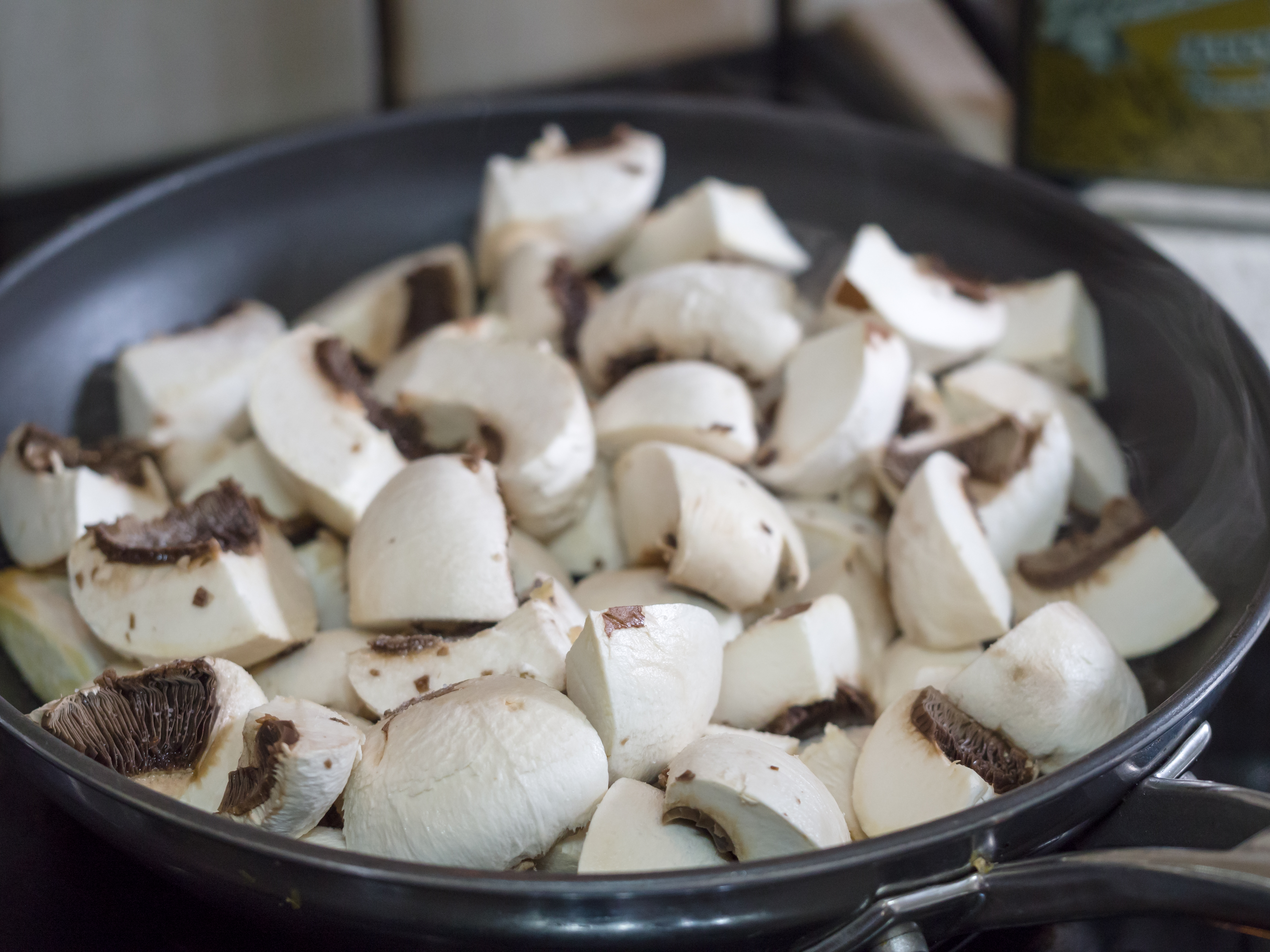 A kitchen frying pan holds several cut up mushrooms.