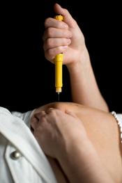 A person is laying with their shirt lifted, so that the stomach is visible. Gripping a syringe full of hormone medication, the needle is pointed towards the pelvic area.