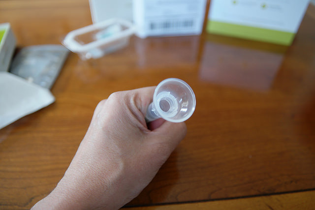 A close-up on a light-skinned hand holding a tube to spit in for sending into a DNA analysis company and getting back results on genetic ancestry.