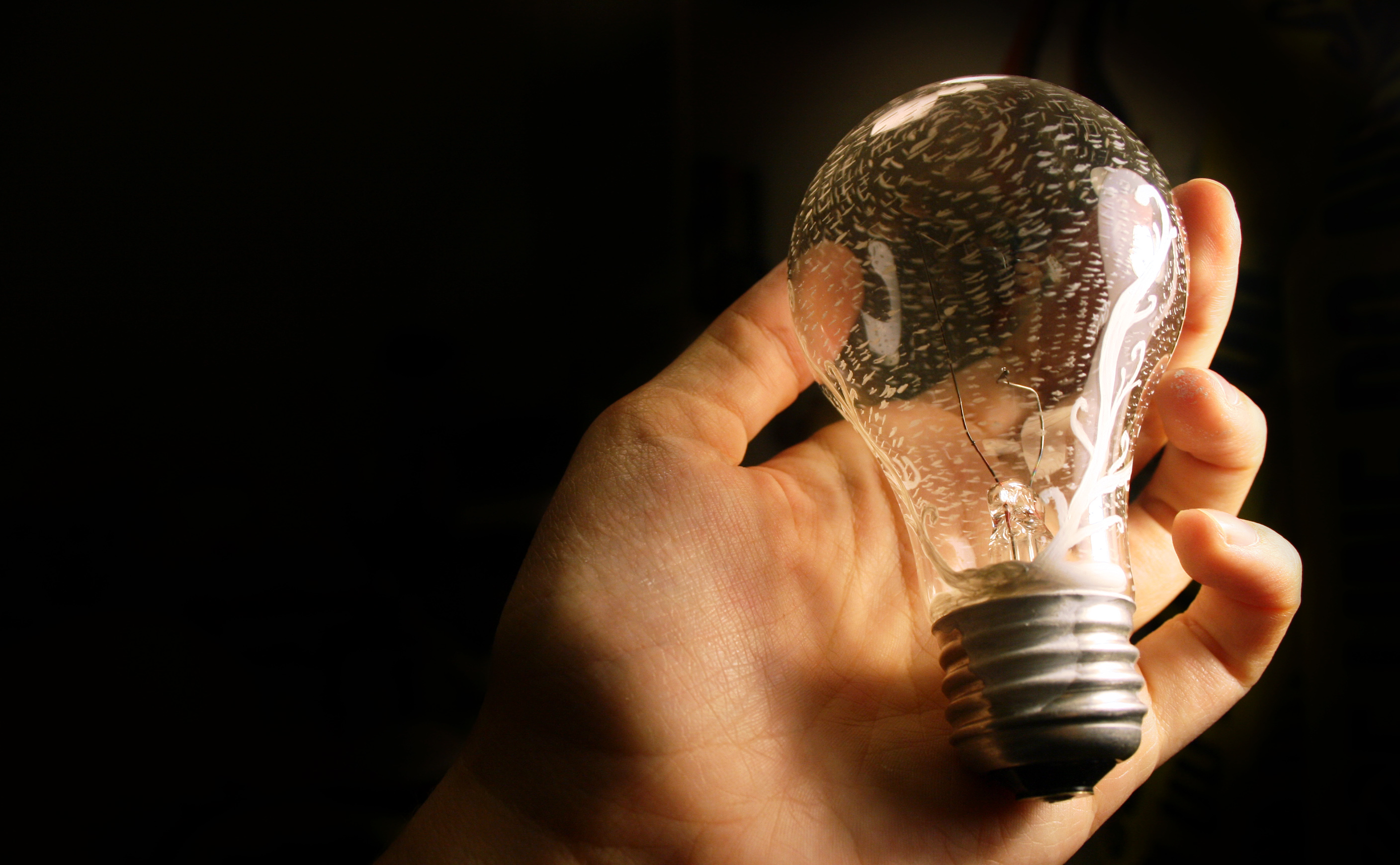 A pale hand holds an unlit light bulb.