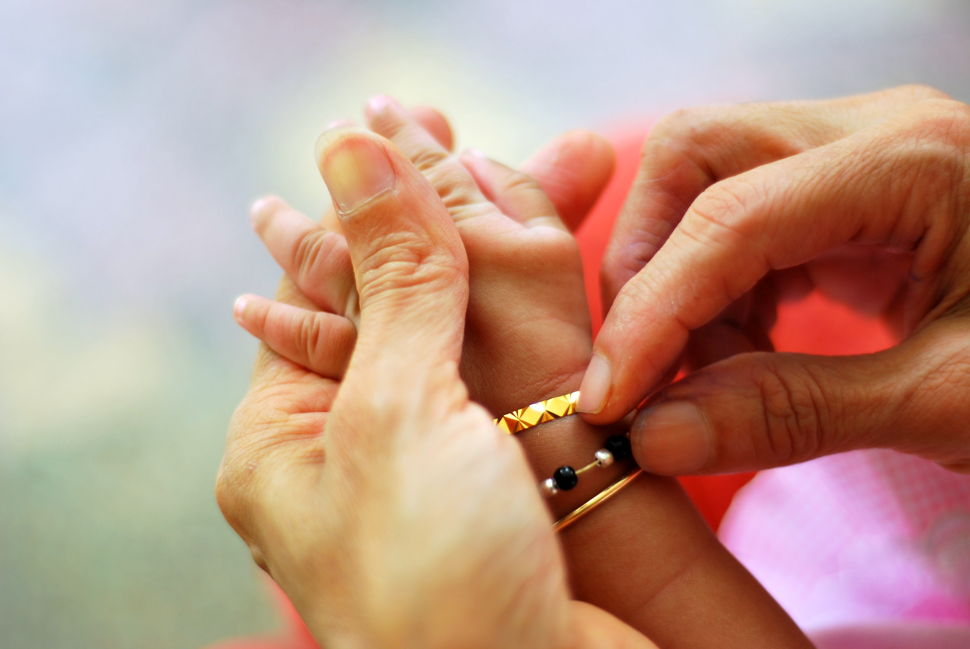 A mother's hands grips a child's hand, who is wearing a bracelet.