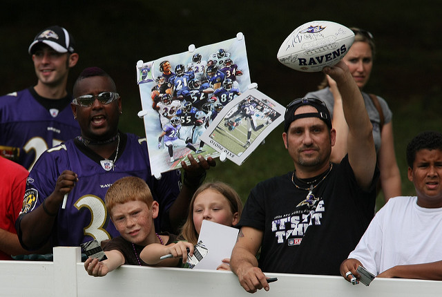 Excited Baltimore Ravens fans are standing behind a fence hoping to get their gear signed.