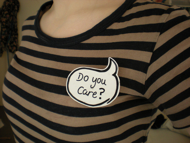 Against a shirt with black and gold stripes, a sticker reads "Do you care?" in a thought/speech bubble.