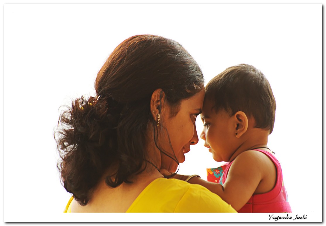 A young mother holds a daughter with their heads gently touching. Their backs are away from the camera.