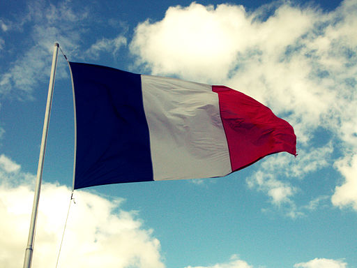 The French flag blows in the wind, against a blue sky with clouds.