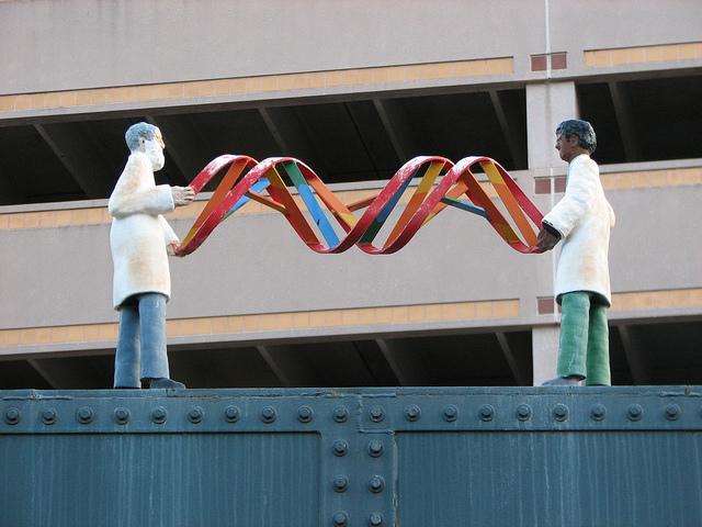 A statue of two male scientists in lab coats. The figures seem to be connected by holding a strand of DNA.
