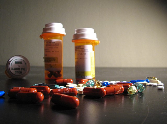 Two upright pill bottles, one pill lying down, and several loose pills, all on top of a black table