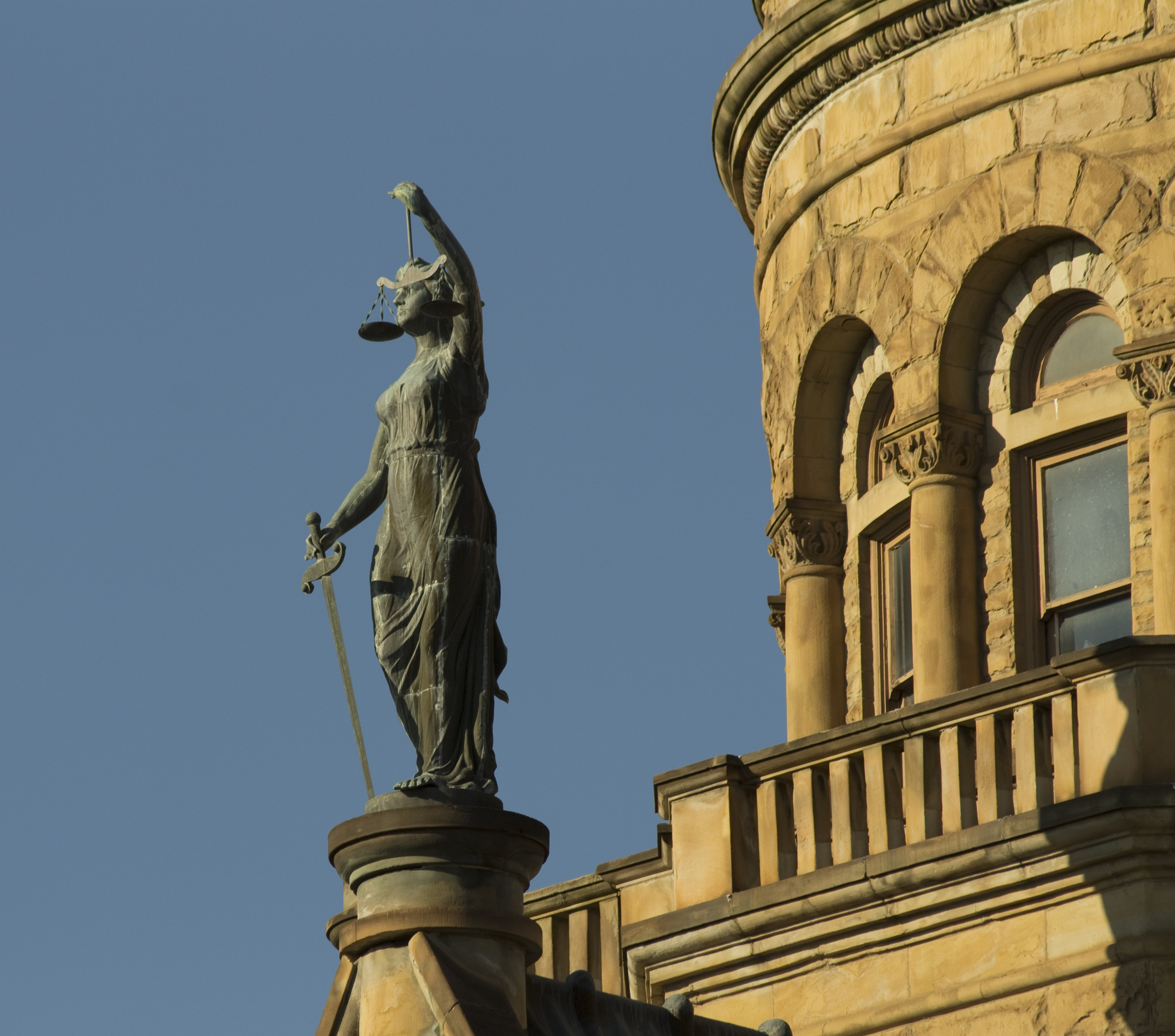 Statue of "Lady of Justice" in front of a courthouse dome.