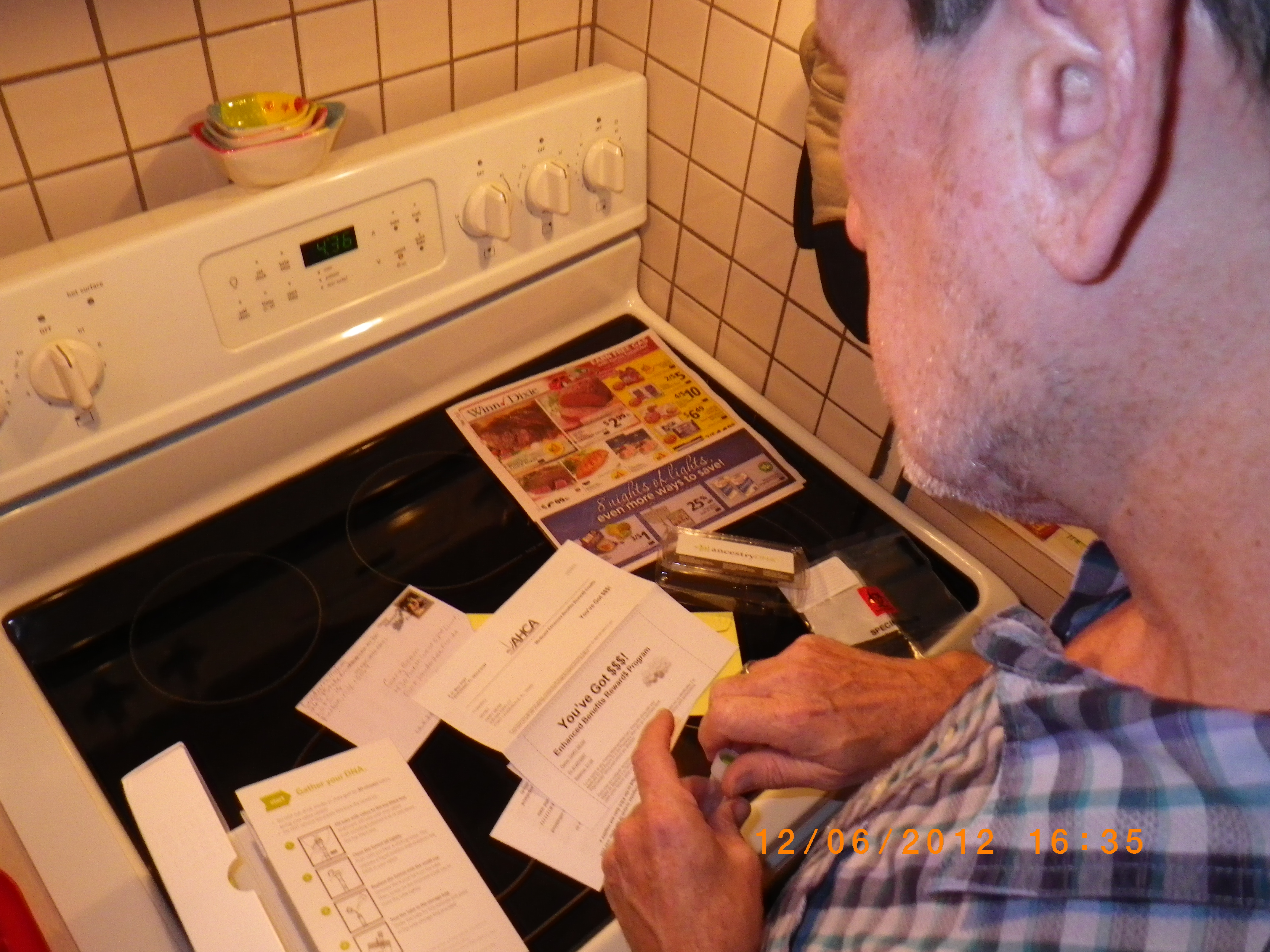 A white male reads over a pile of genetic testing kit contents on a kitchen stove top.