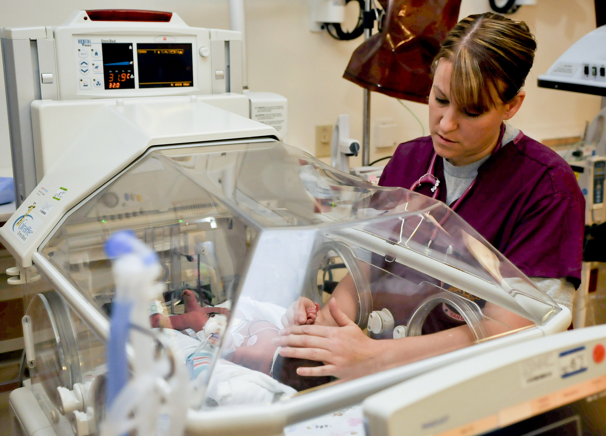 A nurse examines a newborn baby through a transport incubator