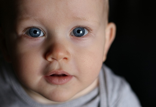 A white infant stares directly, with blue eyes. The baby's mouth is slightly opened.
