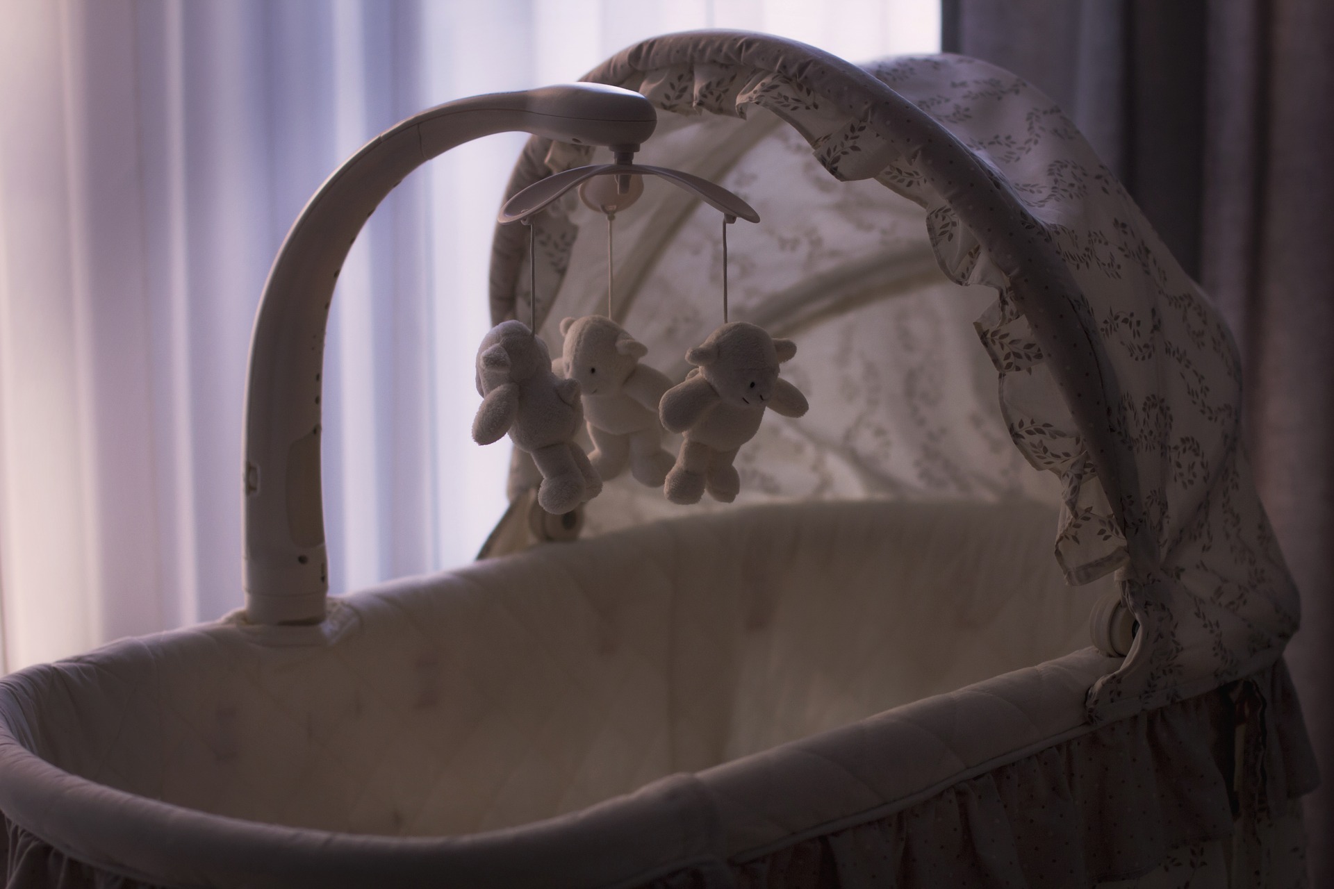 An empty baby cradle, with a spinning mobile of bear toys hanging above.