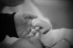 Gray scale photo of an adult's hand holding a baby's.