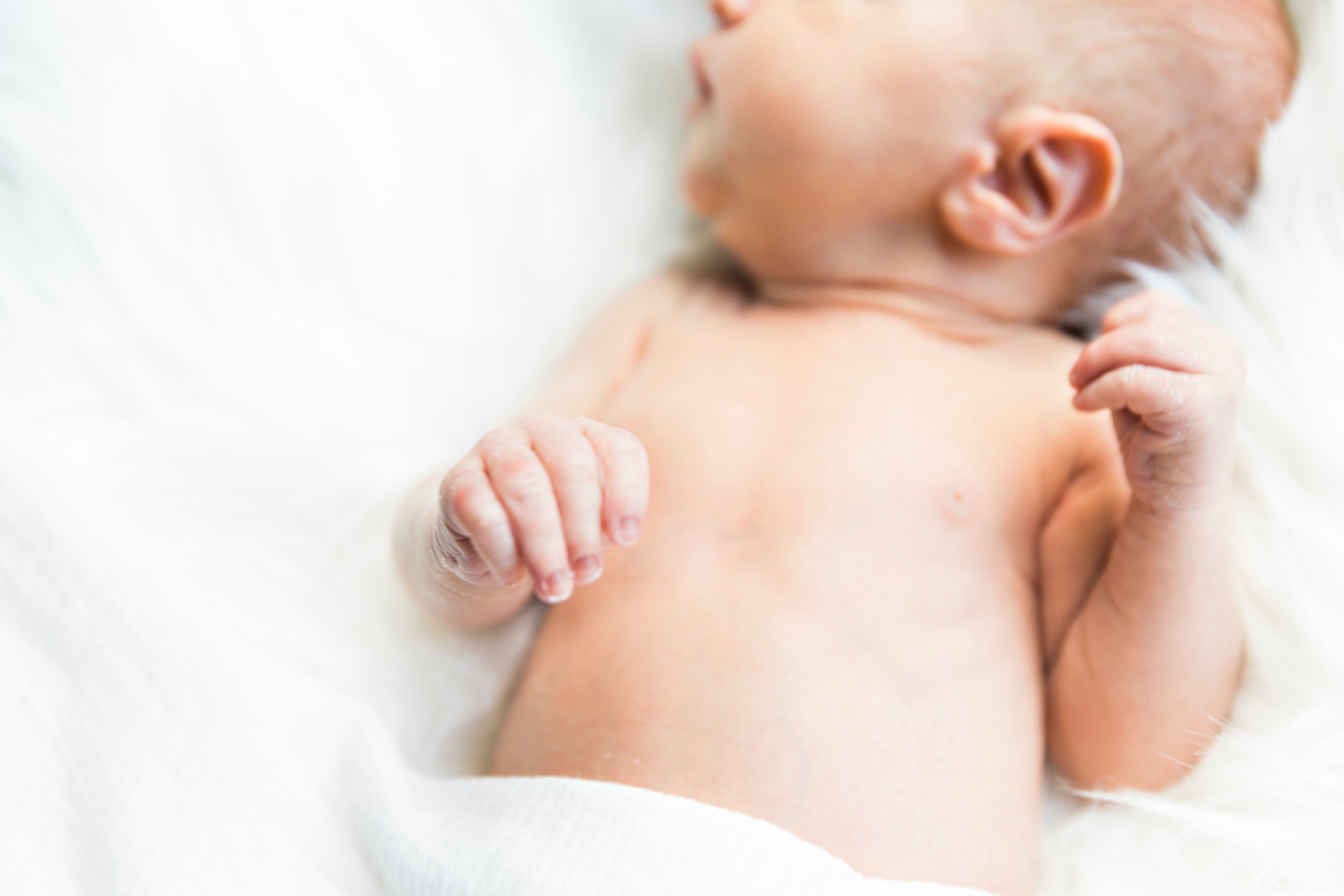 A close-up photograph of a light-skinned newborn baby with its face obscured