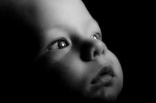Black and white photo of a young baby looking out distantly.