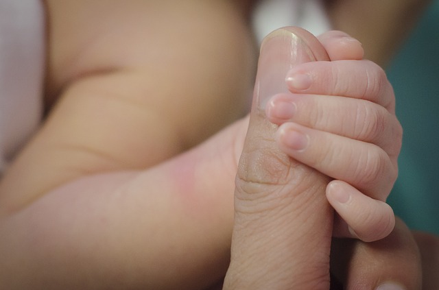 A baby's fingers grasps an adult's finger.