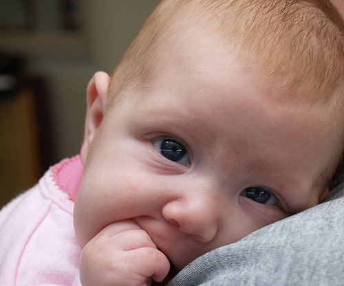 Baby in pink shirt with hand in its mouth