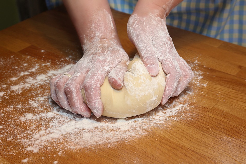 Two dusted hands knead dough on a floured wooden counter.