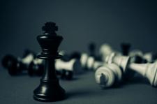 Several chess pieces are photographed in black and white, with an emphasized black king piece standing tall.