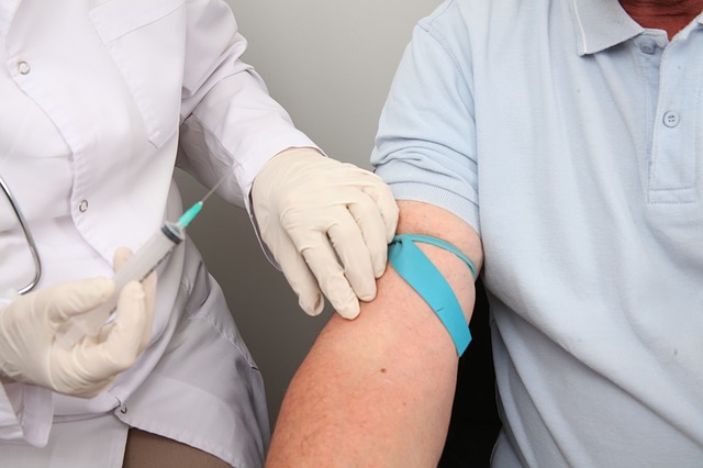A medical expert wearing gloves and a white coat, hold a needle as a patient extends their arm.