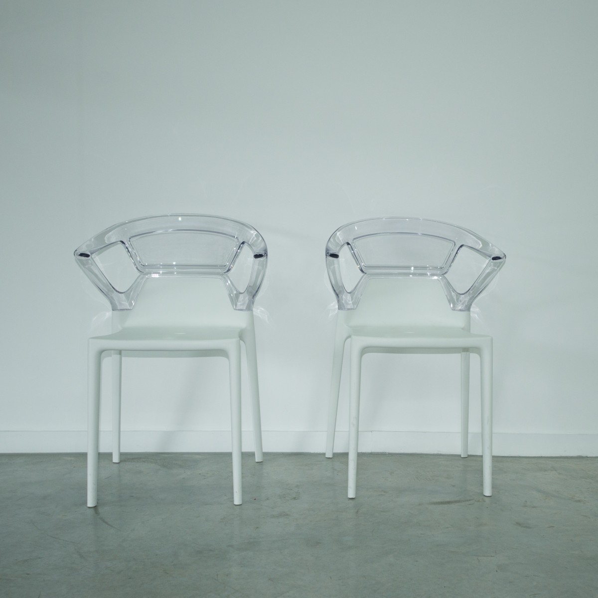 Two clear chairs sit side by side against a white wall.