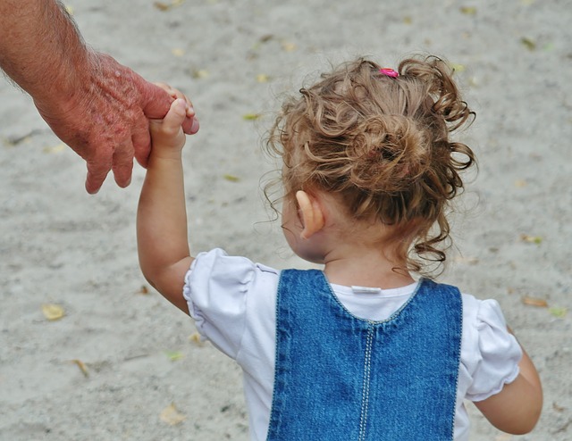 A small child with curly hair holds a finger on an adult's hand