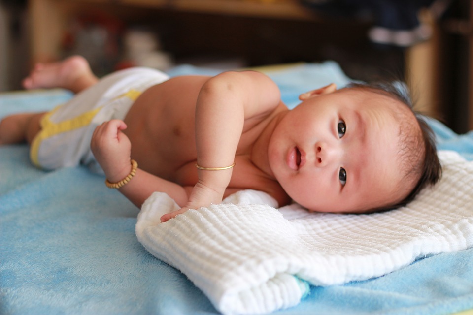 Newborn baby lying on white towel on blue hospital bed 