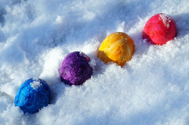 A row of brightly colored blue, purple, yellow and red eggs sits in the snow