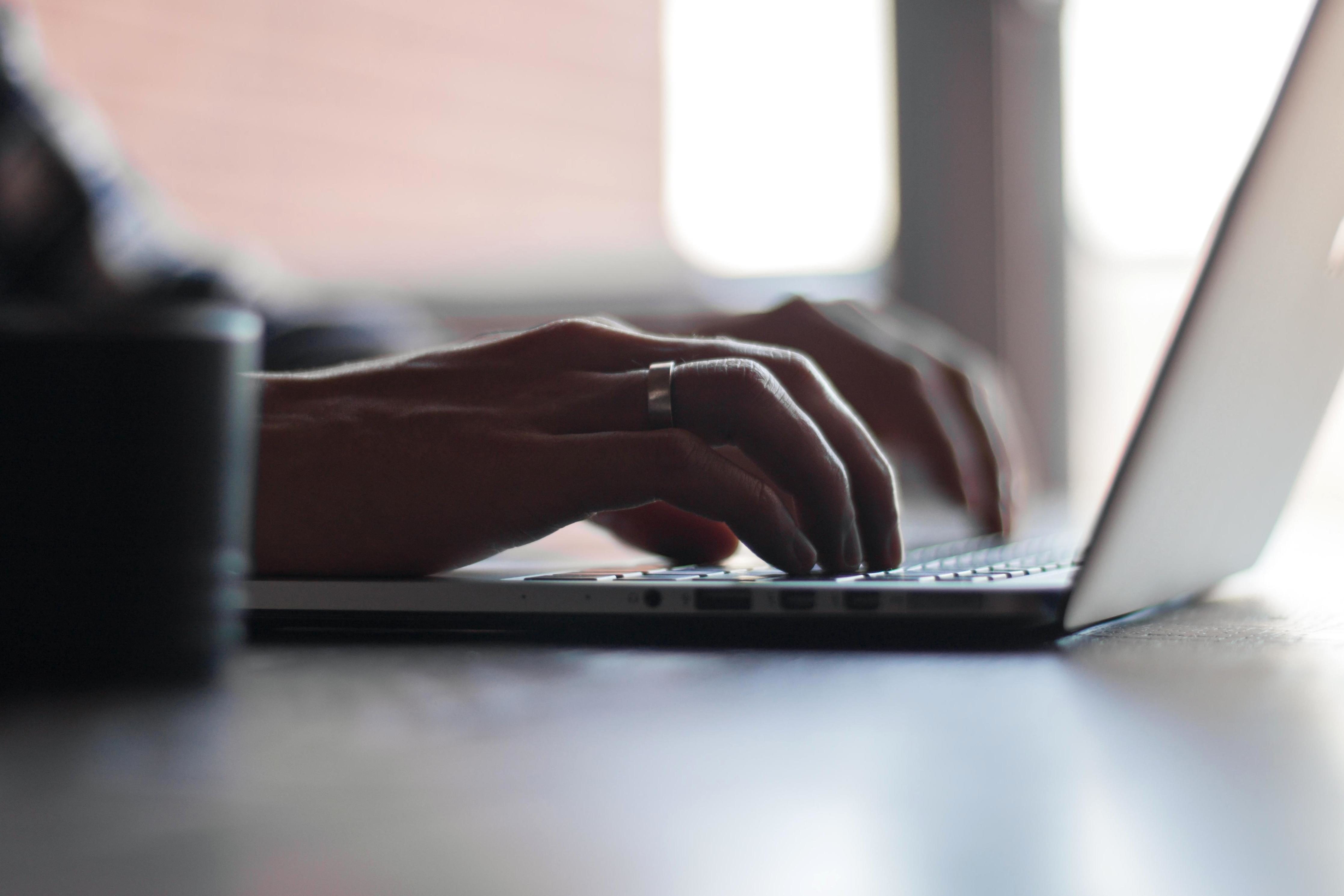 Close up of a man's hands typing on a laptop.