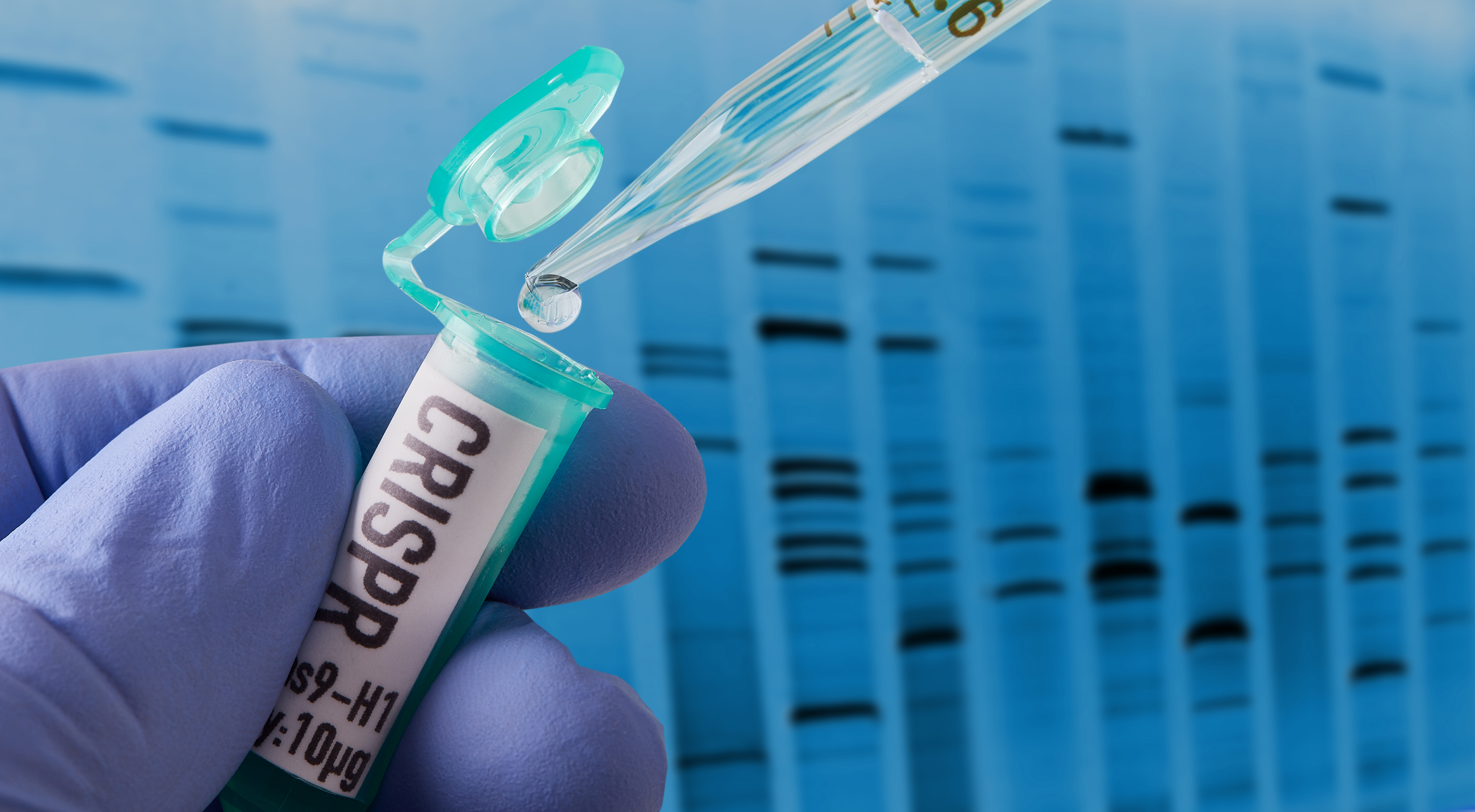 A gloved hand drops material to a vial labeled CRISPR