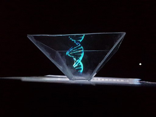 Spotlighted against a black shadowy background is a blue DNA model projected by an upside down shaped pyramid hologram