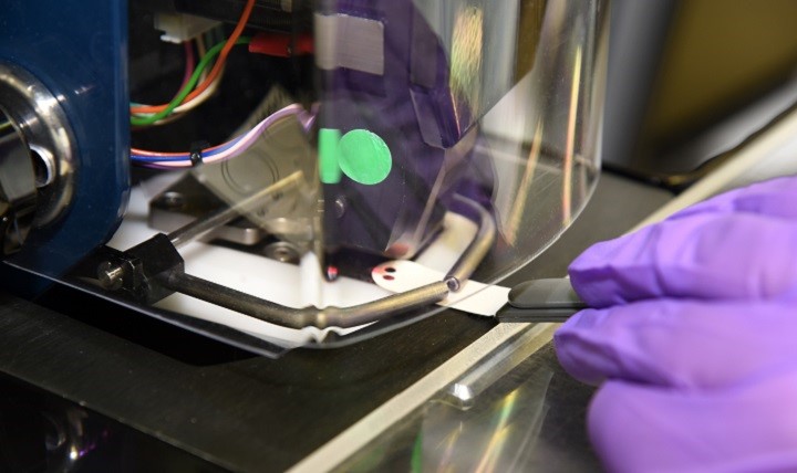 A purple-gloved hand inserts a piece of paper into a machine to extract DNA from the swab.