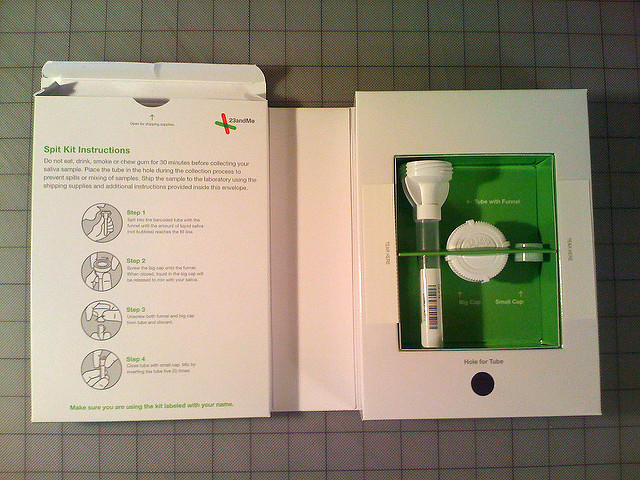 the contents of a 23 and Me test kit: test tube with funnel and two white caps in a white and green box