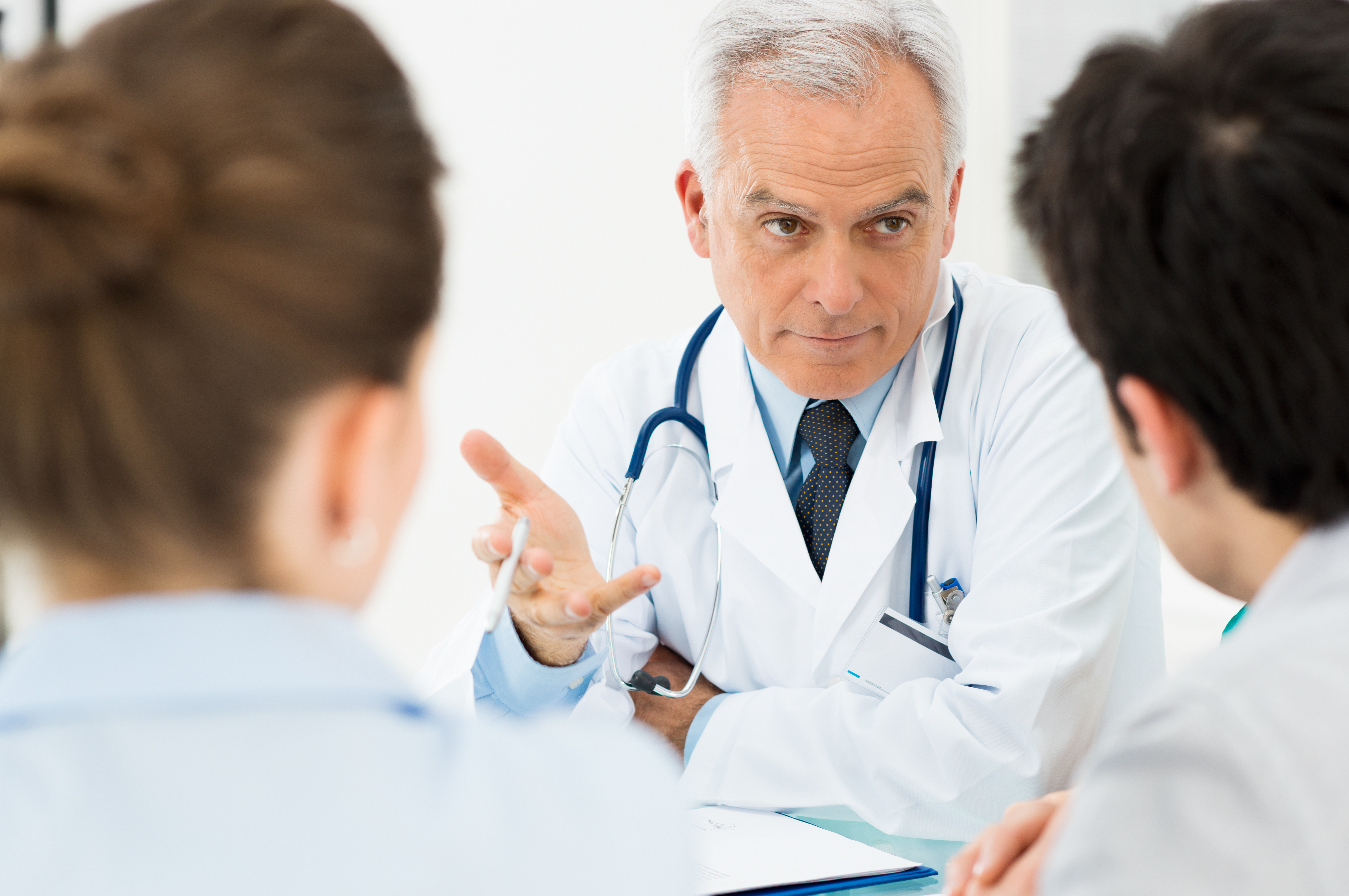 a doctor with white hair explains a medical procedure to a young white couple with brown hair