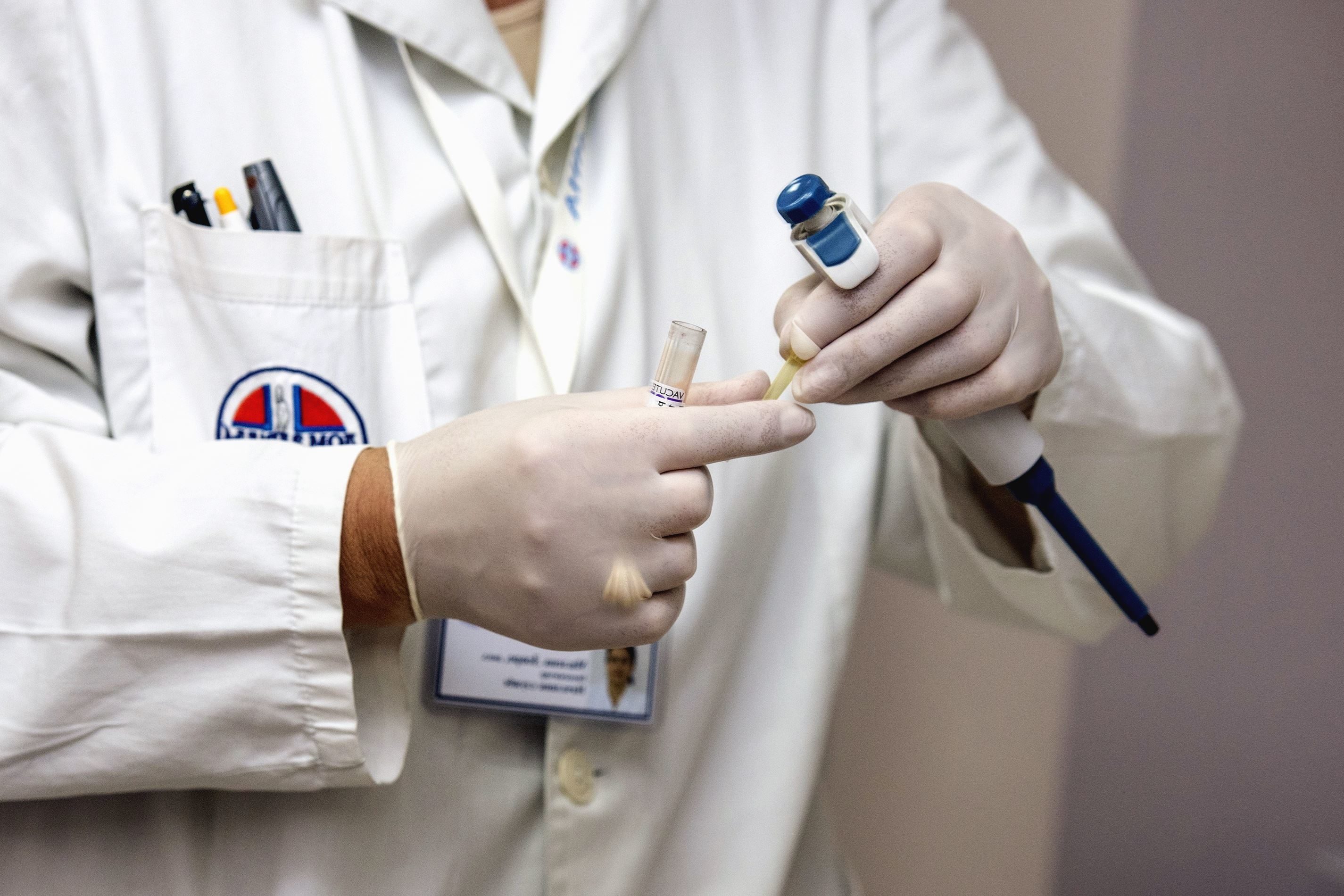 Close up of doctor's gloved hands holding a pipette and a test tube.