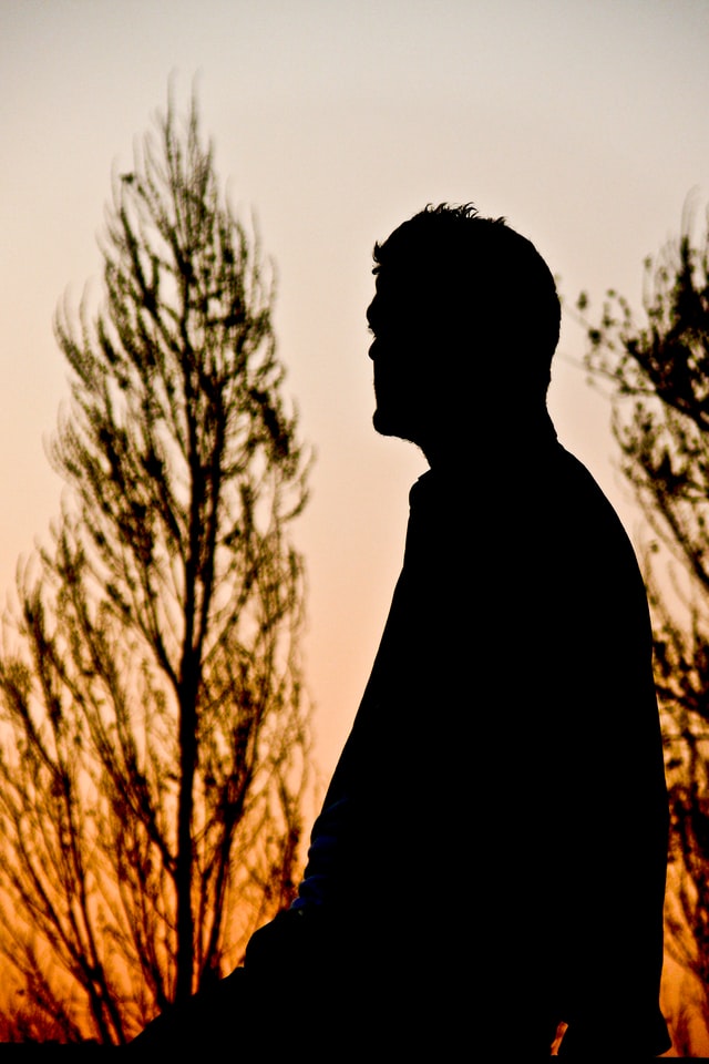 silhouette of a seated man with trees in background