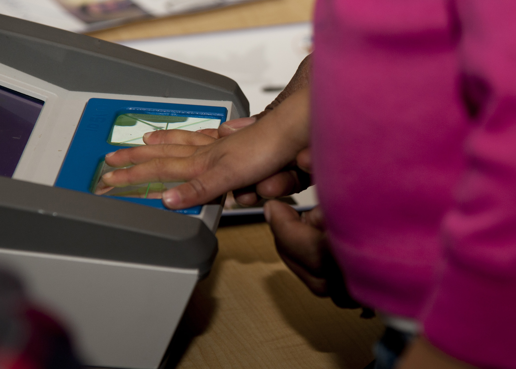 An individual's hand is held to a scanning machine for fingerprinting.