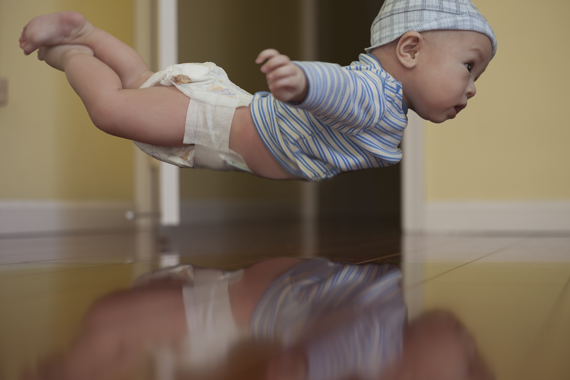 A baby dressed in a shirt, diapers, and cap, floats mid-air.